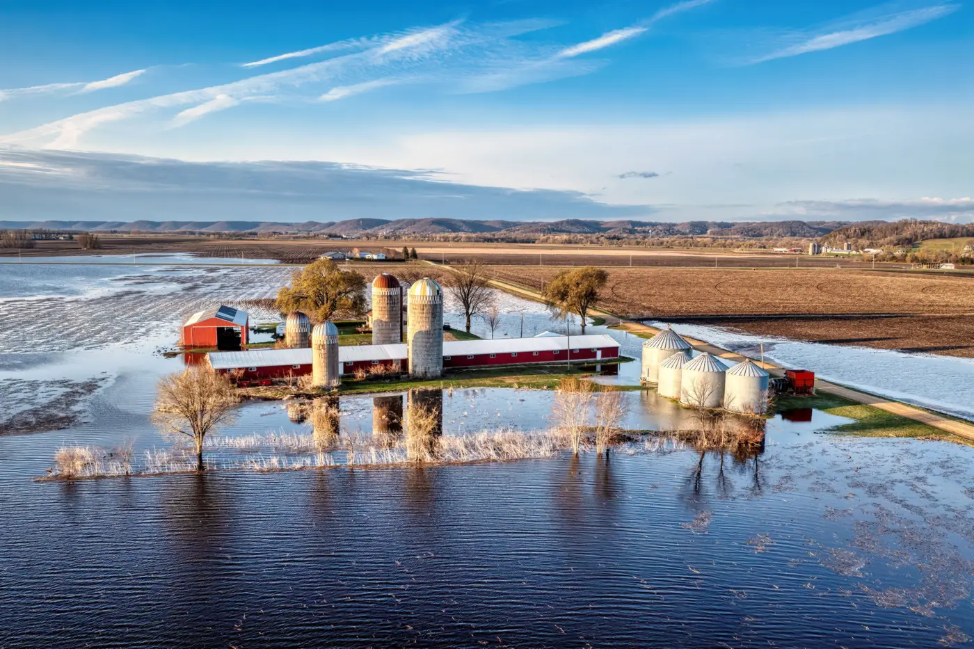 Aerial view of a farm with barns and grain silos surrounded by flood water